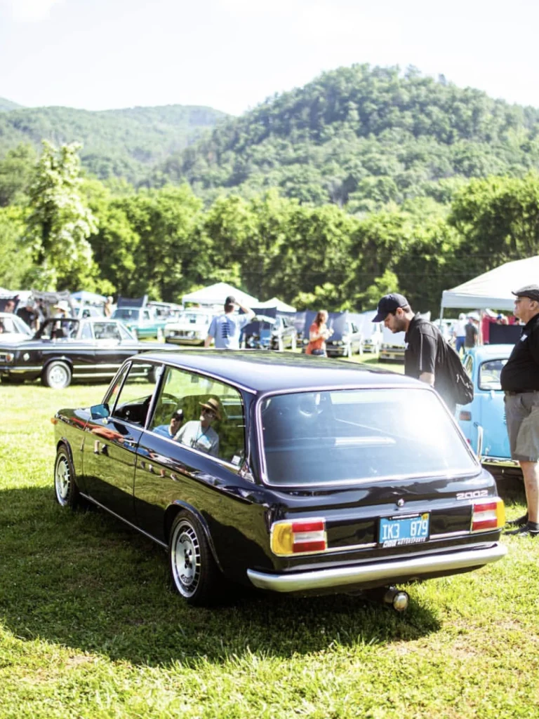 Rear three-quarter view of a dark classic BMW parked on grass at an outdoor car gathering.