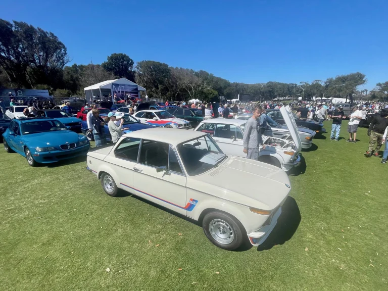 Cream-colored classic BMW among rows of cars and visitors at an outdoor car gathering.