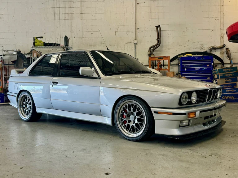 White BMW coupe with multi-spoke wheels parked inside the workshop beside tool chests.