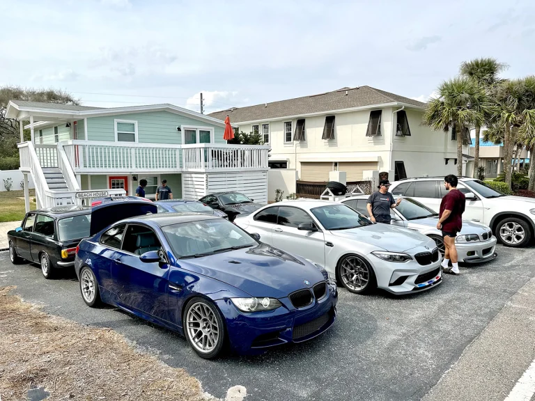 Blue and white BMW coupes with other cars and people parked outside residential buildings.