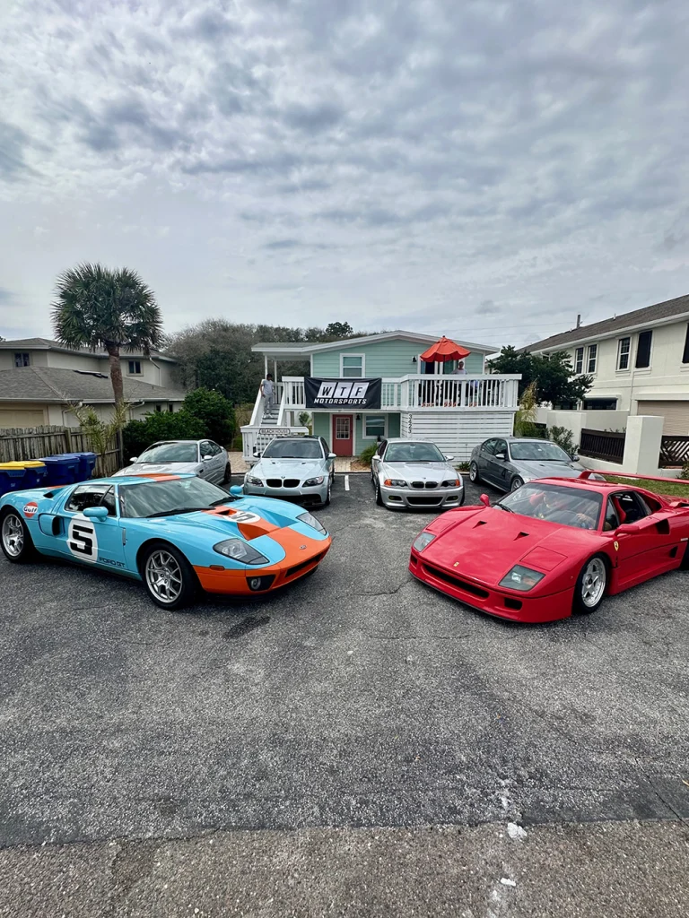 Blue and orange number 5 sports car and red sports car parked with other vehicles outside a building.
