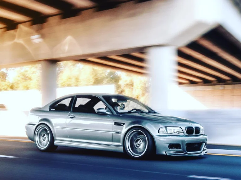 Silver BMW coupe driving beneath a concrete overpass.