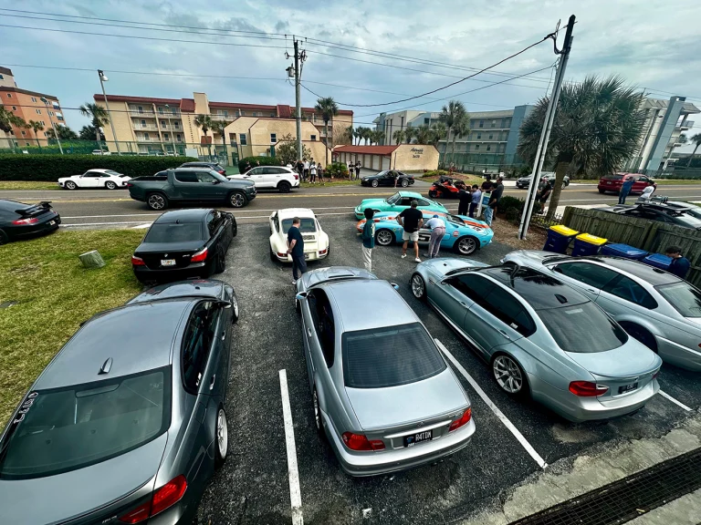 Elevated view of cars and people gathered in a parking lot beside a street.